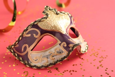 Photo of Beautiful carnival mask with party decor on coral background, closeup