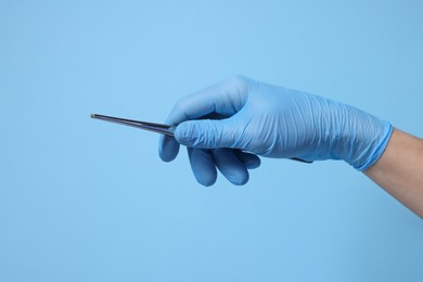 Doctor wearing medical glove holding tweezers on light blue background, closeup