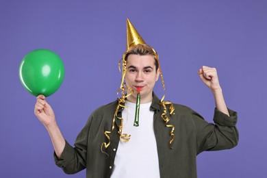 Young man with party hat, blower and balloon on purple background