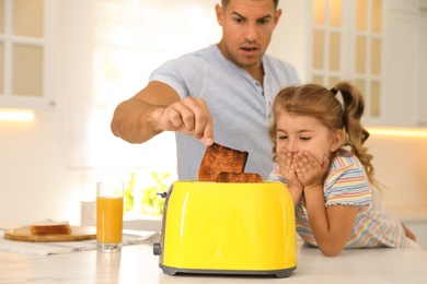 Emotional father and daughter near toaster with slices of burnt bread in kitchen