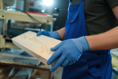 Photo of Professional carpenter with wooden board in workshop, closeup