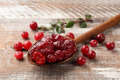 Tasty dried cranberries in spoon and fresh ones on rustic wooden table, closeup