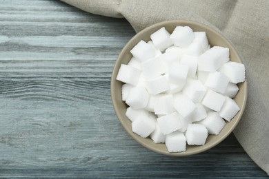 Photo of White sugar cubes in bowl on wooden table, top view. Space for text