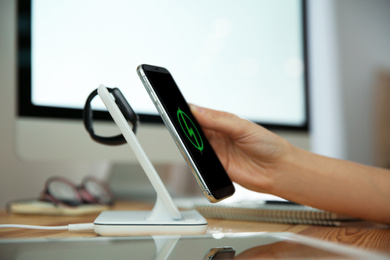 Woman putting mobile phone onto wireless charger at wooden table, closeup. Modern workplace accessory