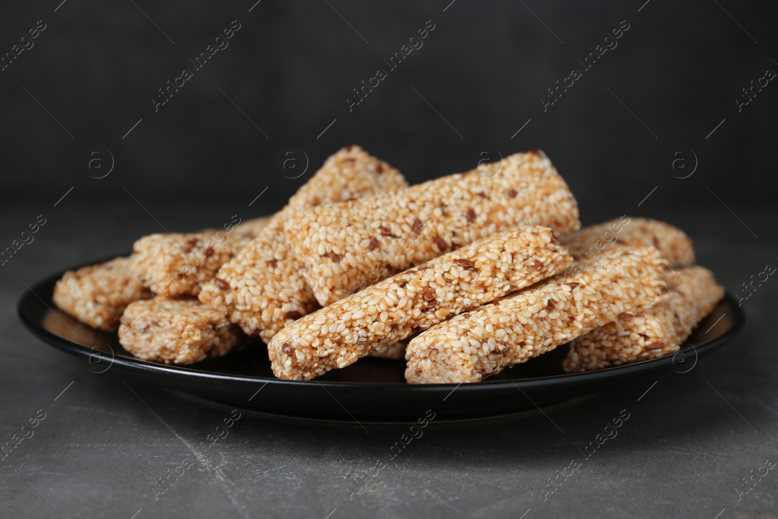 Photo of Plate with tasty sesame seed bars on dark grey table
