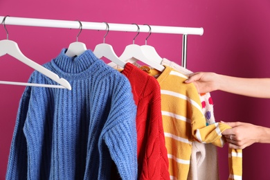 Woman choosing sweater on rack against color background