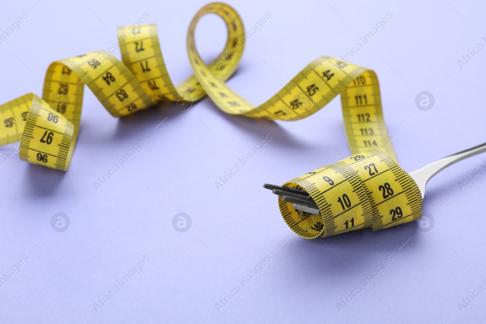 Photo of Fork with measuring tape on violet background, closeup. Diet concept