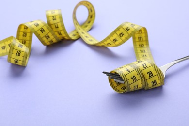 Fork with measuring tape on violet background, closeup. Diet concept