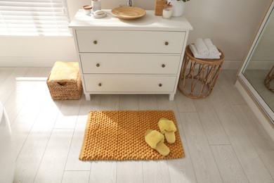 Photo of Stylish orange mat with slippers near chest of drawers in bathroom