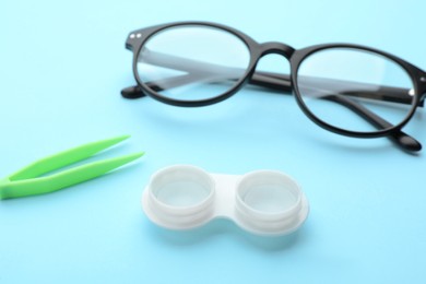 Photo of Case with contact lenses, glasses and tweezers on light blue background