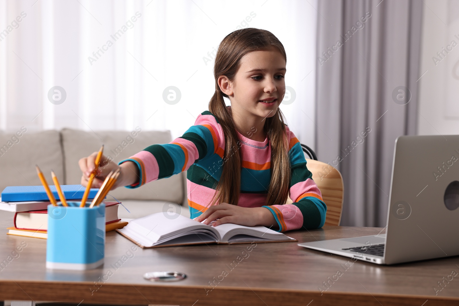 Photo of E-learning. Cute girl using laptop during online lesson at table indoors