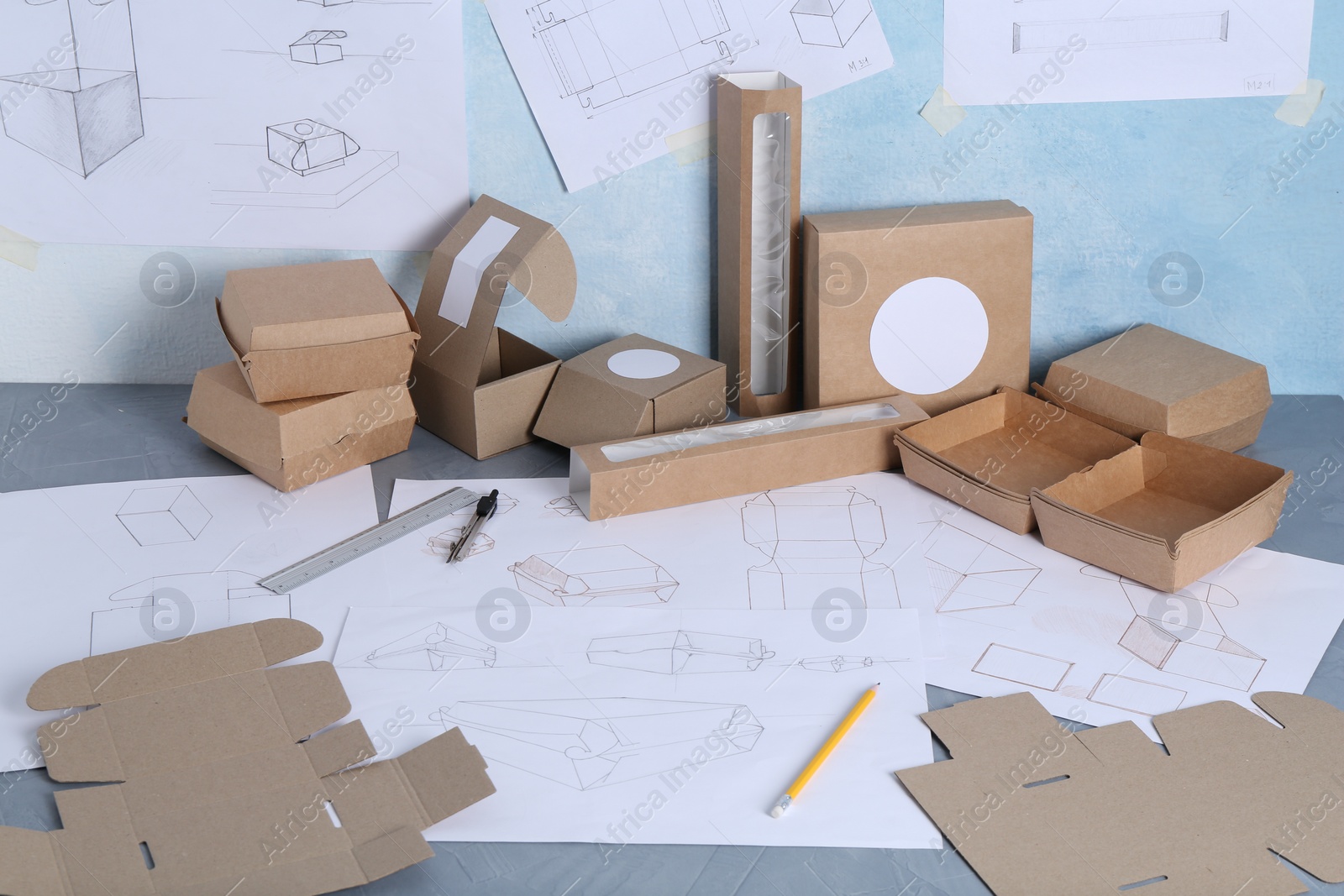 Photo of Creating packaging design. Drawings, boxes and stationery on blue textured table, closeup