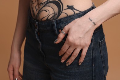 Photo of Woman with cool tattoos on beige background, closeup