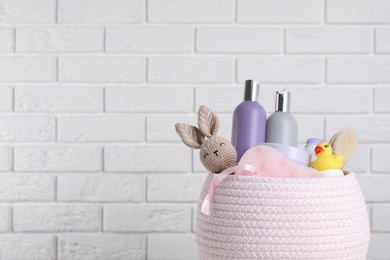 Photo of Basket full of different baby cosmetic products, accessories and toys against white brick wall. Space for text