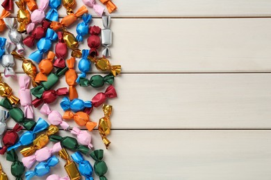 Photo of Candies in colorful wrappers on beige wooden table, flat lay. Space for text