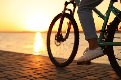Woman riding bicycle on embankment at sunset, closeup