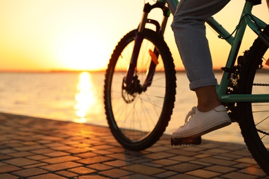 Photo of Woman riding bicycle on embankment at sunset, closeup