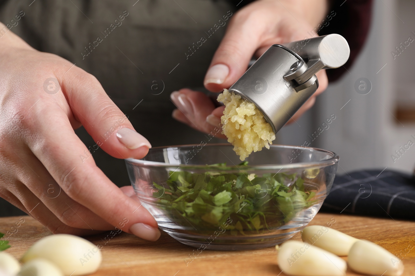 Photo of Woman squeezing garlic with press at wooden table indoors, closeup