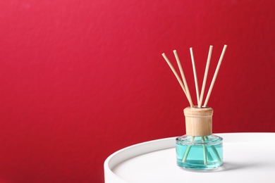 Photo of Reed air freshener on white table against red background, space for text