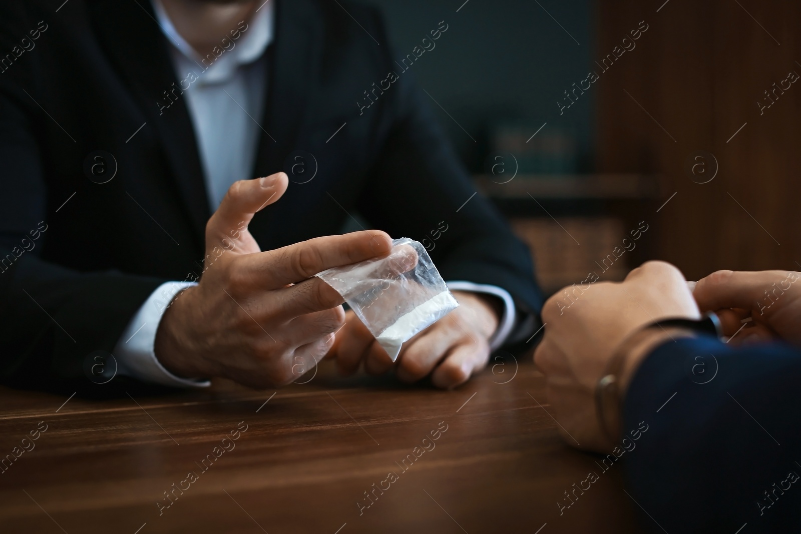 Photo of Police officer interrogating drug dealer in handcuffs at desk indoors. Criminal law