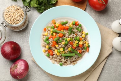 Photo of Tasty pearl barley porridge with vegetables on light textured table, flat lay