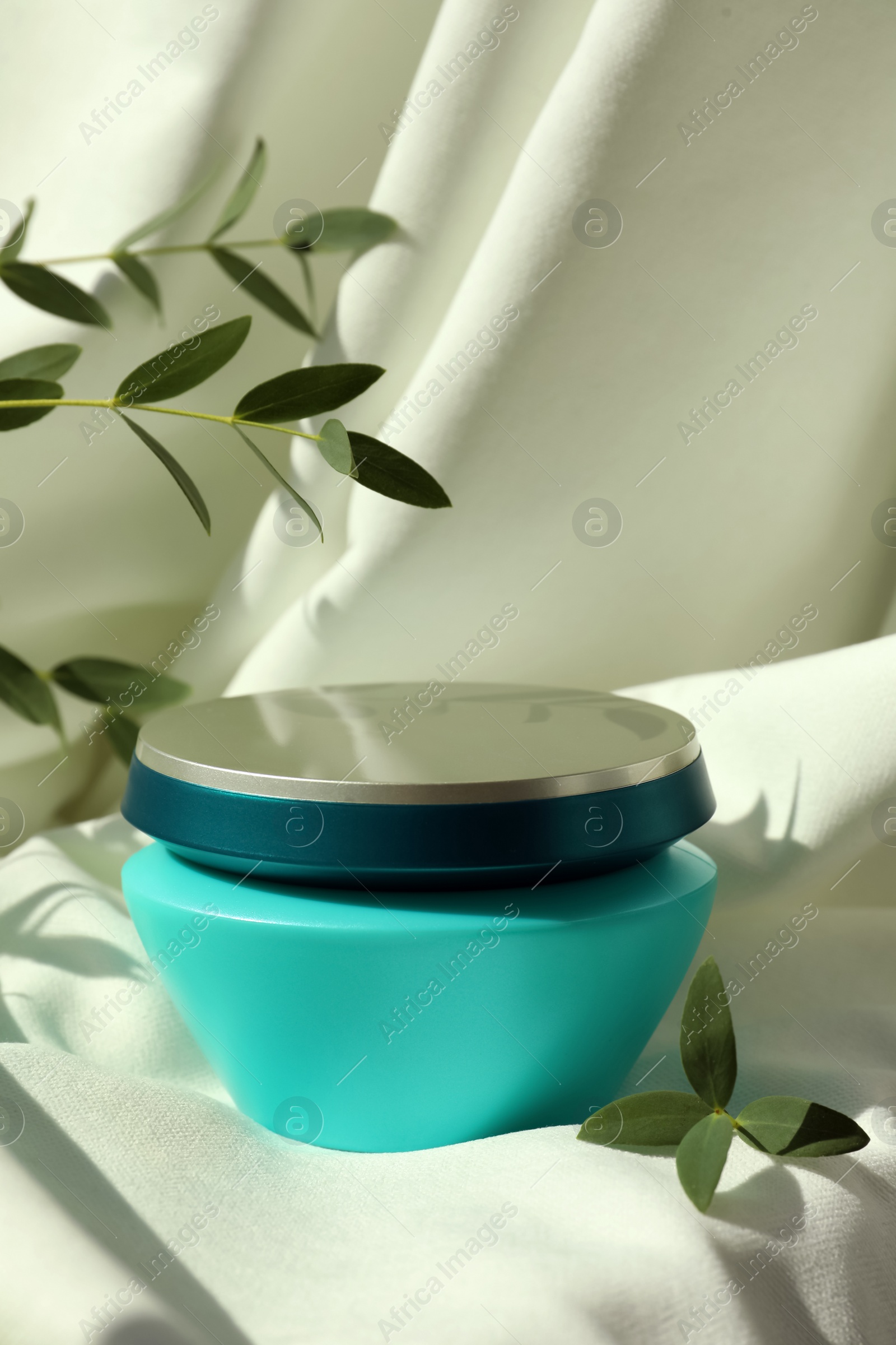 Photo of Jar of hair care cosmetic product and green leaves on light fabric