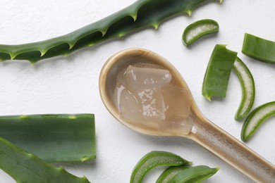 Photo of Aloe vera gel in spoon and slices of plant on white background, flat lay