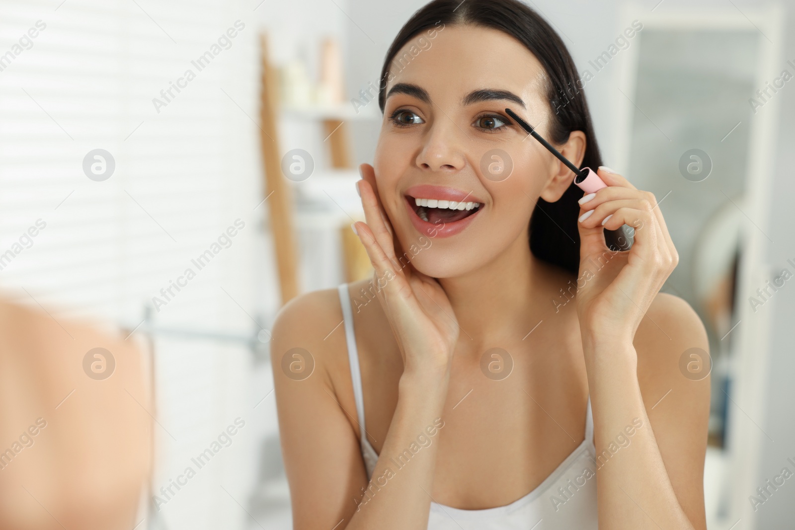 Photo of Beautiful young woman applying mascara in bathroom