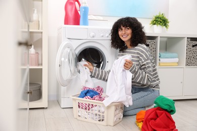 Photo of Happy woman putting laundry into washing machine indoors