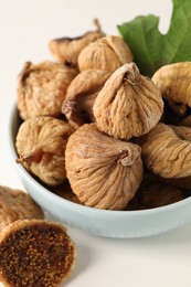 Bowl with tasty dried figs and green leaf on white wooden table, closeup