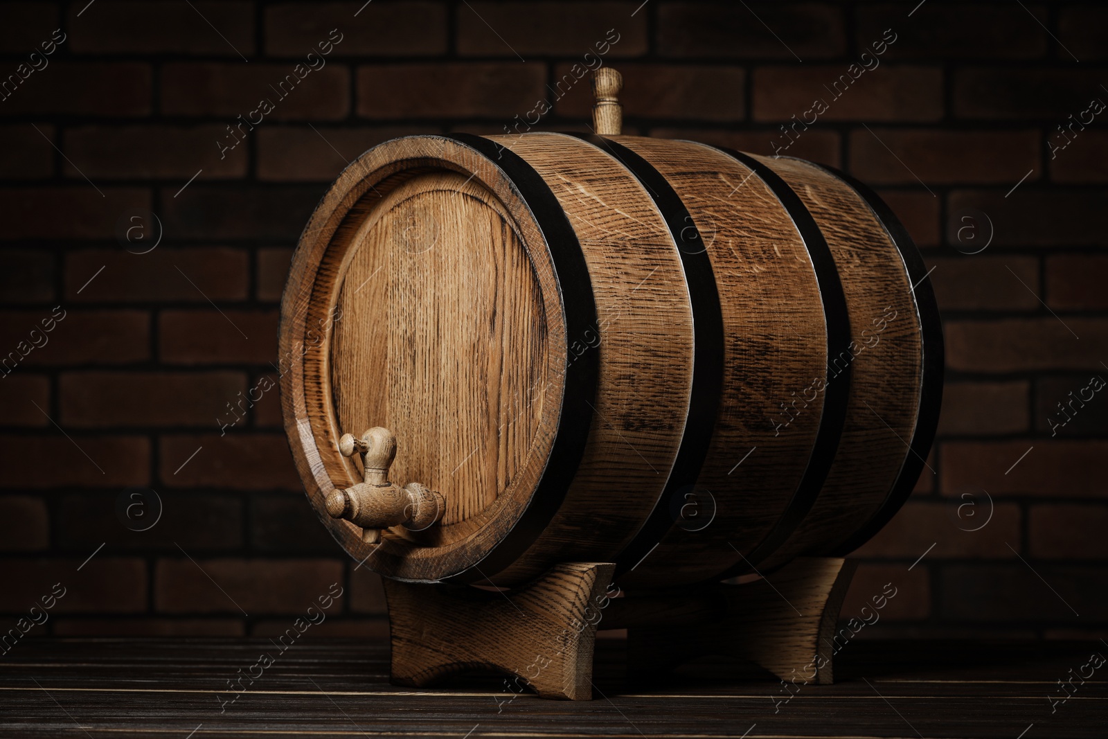 Photo of Wooden barrel with tap on table near brick wall