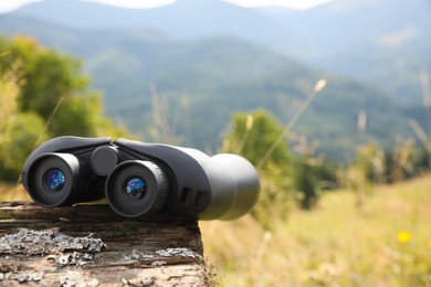 Photo of Modern binoculars on wooden log outdoors, space for text