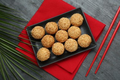 Photo of Delicious sesame balls, green leaf, chopsticks on black table, flat lay