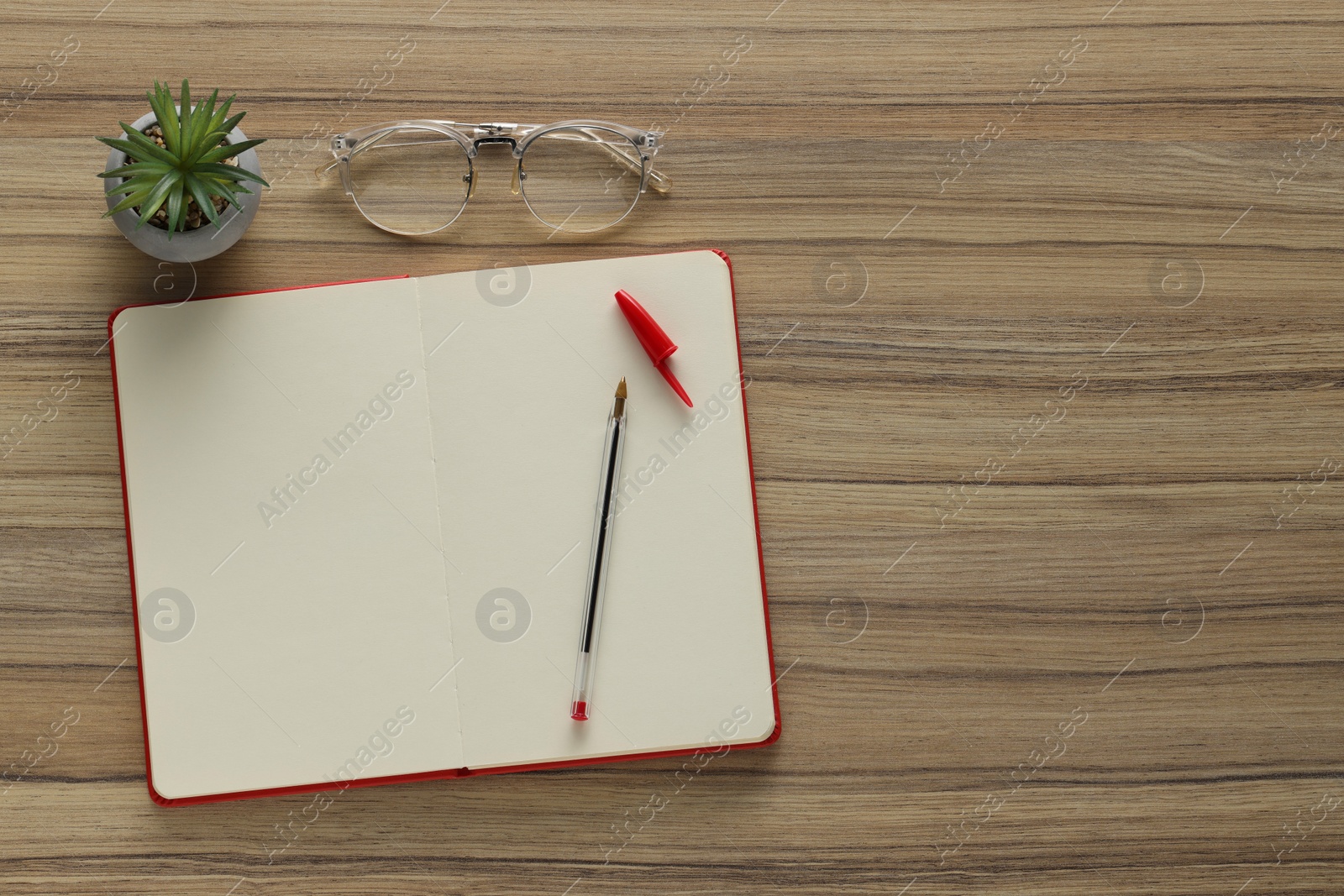 Photo of Ballpoint pen, notebook and glasses on wooden table, flat lay. Space for text