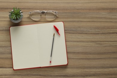 Photo of Ballpoint pen, notebook and glasses on wooden table, flat lay. Space for text