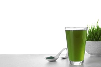 Glass of spirulina drink and spoon with powder on table against white background. Space for text