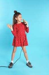 Cute funny girl with microphone on color background