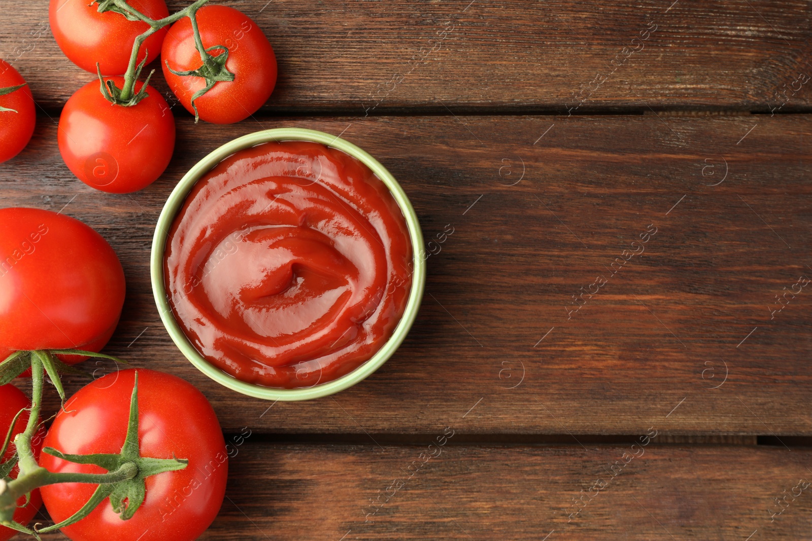 Photo of Bowl of tasty ketchup and tomatoes on wooden table, flat lay. Space for text