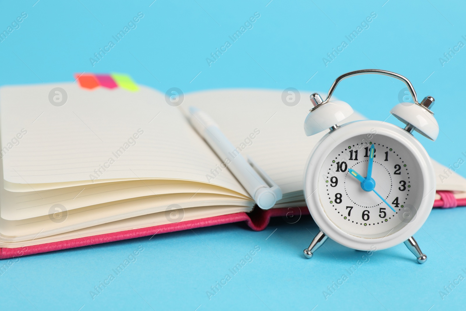 Photo of Alarm clock, pen and open notebook on light blue background. Reminder concept