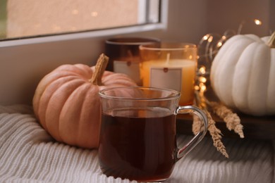 Cup of hot drink, candles, pumpkins and white knitted blanket on window sill indoors