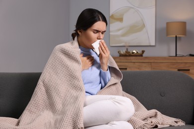 Photo of Woman coughing with tissue on sofa at home. Cold symptoms