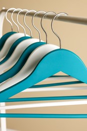 Clothes hangers on metal rail against beige background, closeup view