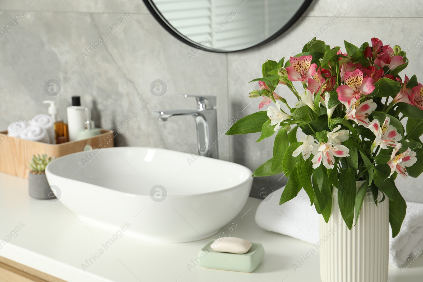 Photo of Vase with beautiful Alstroemeria flowers and toiletries near sink in bathroom