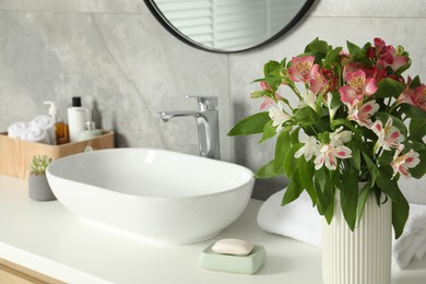 Photo of Vase with beautiful Alstroemeria flowers and toiletries near sink in bathroom