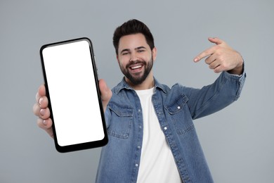 Happy man holding smartphone with empty screen on grey background