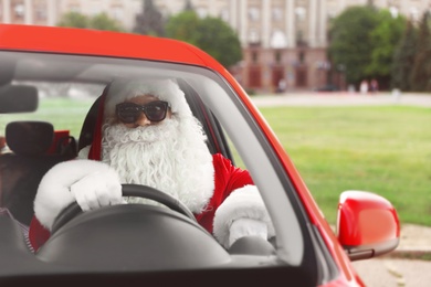 Authentic Santa Claus in sunglasses driving car, view from outside