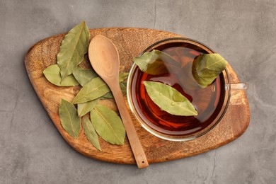 Photo of Cup of freshly brewed tea with bay leaves on grey table, top view