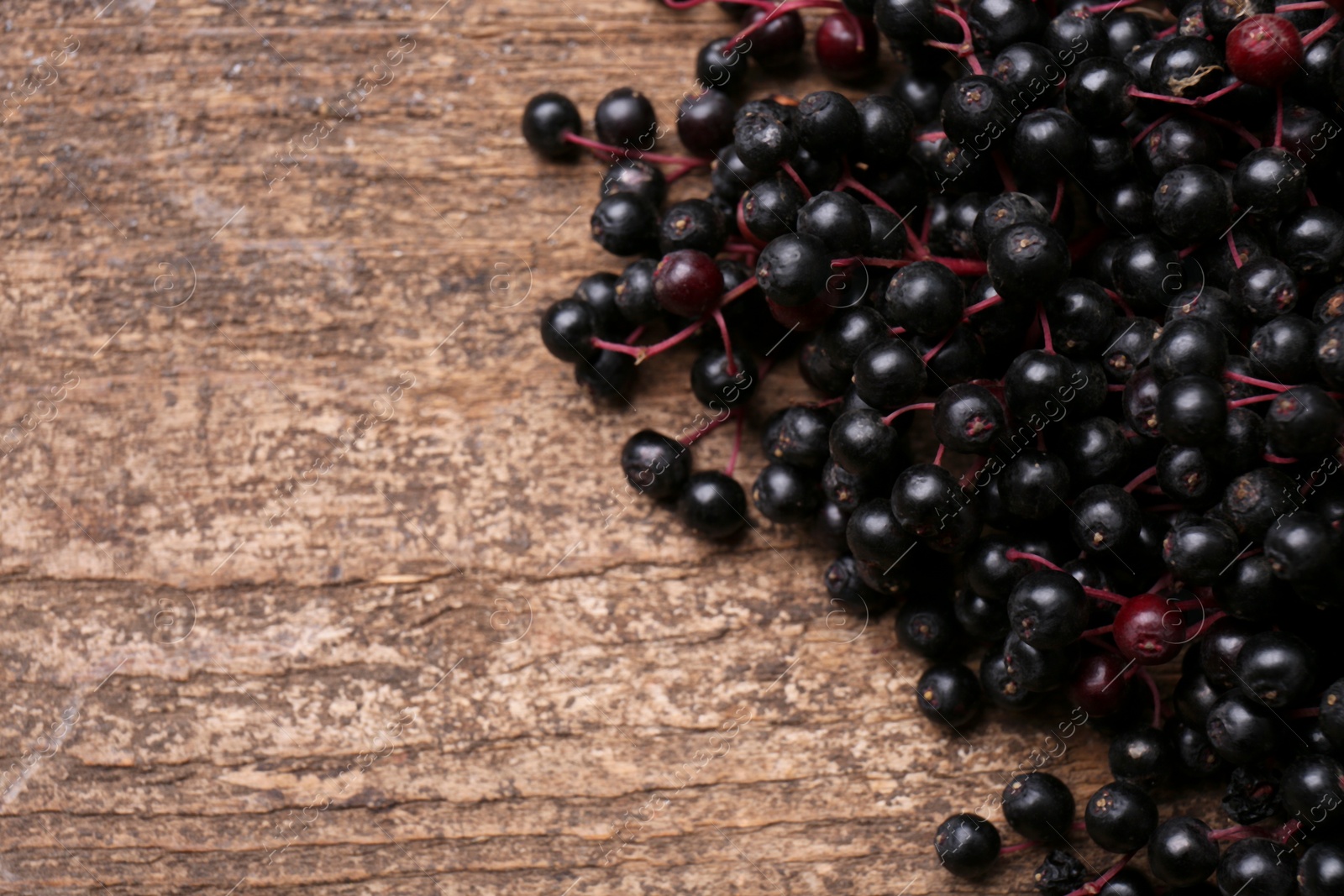 Photo of Pile of tasty elderberries (Sambucus) on wooden table, closeup. Space for text