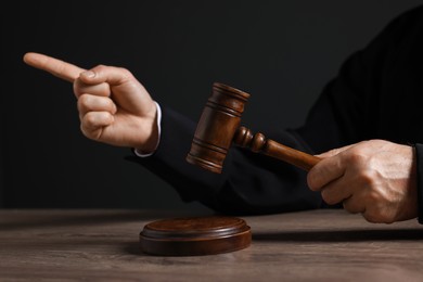 Photo of Judge with gavel pointing at wooden table against black background, closeup