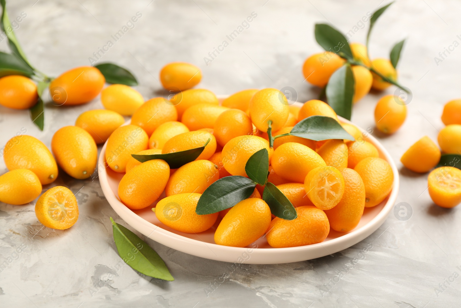 Photo of Fresh ripe kumquats in plate on light grey table